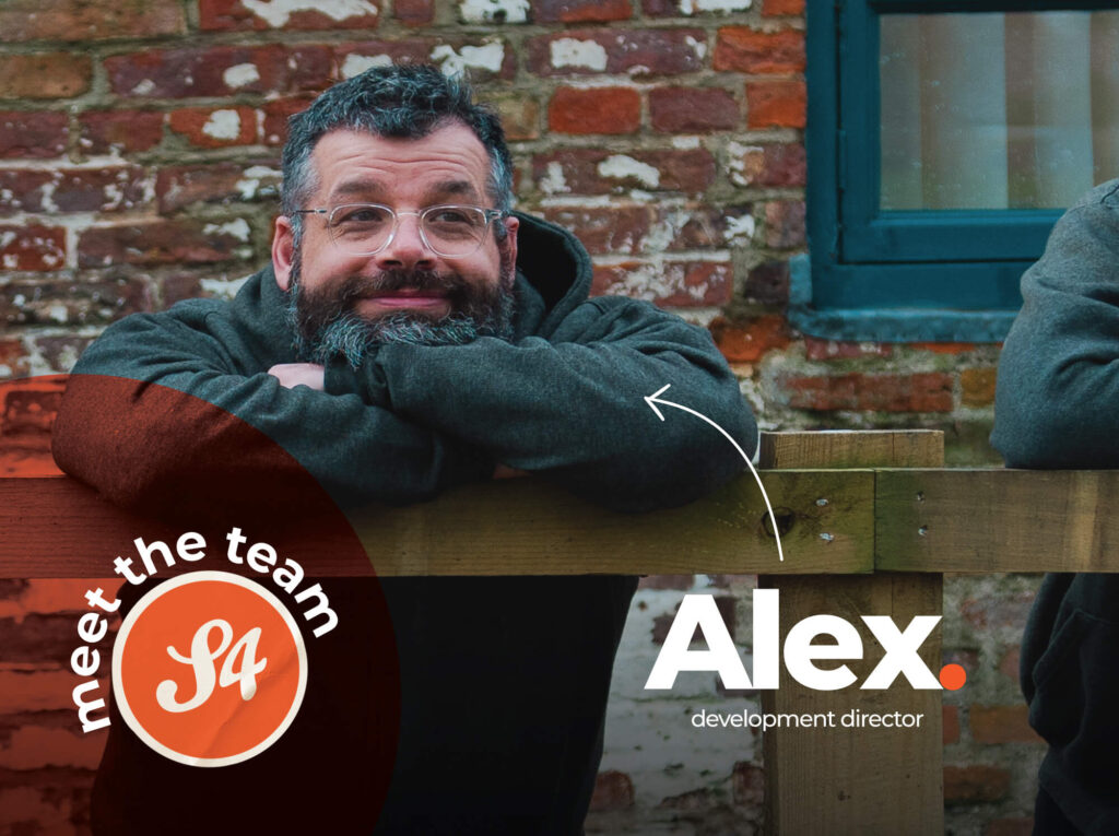 Meet the S4 Team - Sourcefour Development Director Alex leaning on a wooden fence outside of the studio, in front of a brick wall