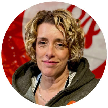 A person with short curly hair is wearing a jacket in front of an "About Us" backdrop, featuring striking red and white colors.